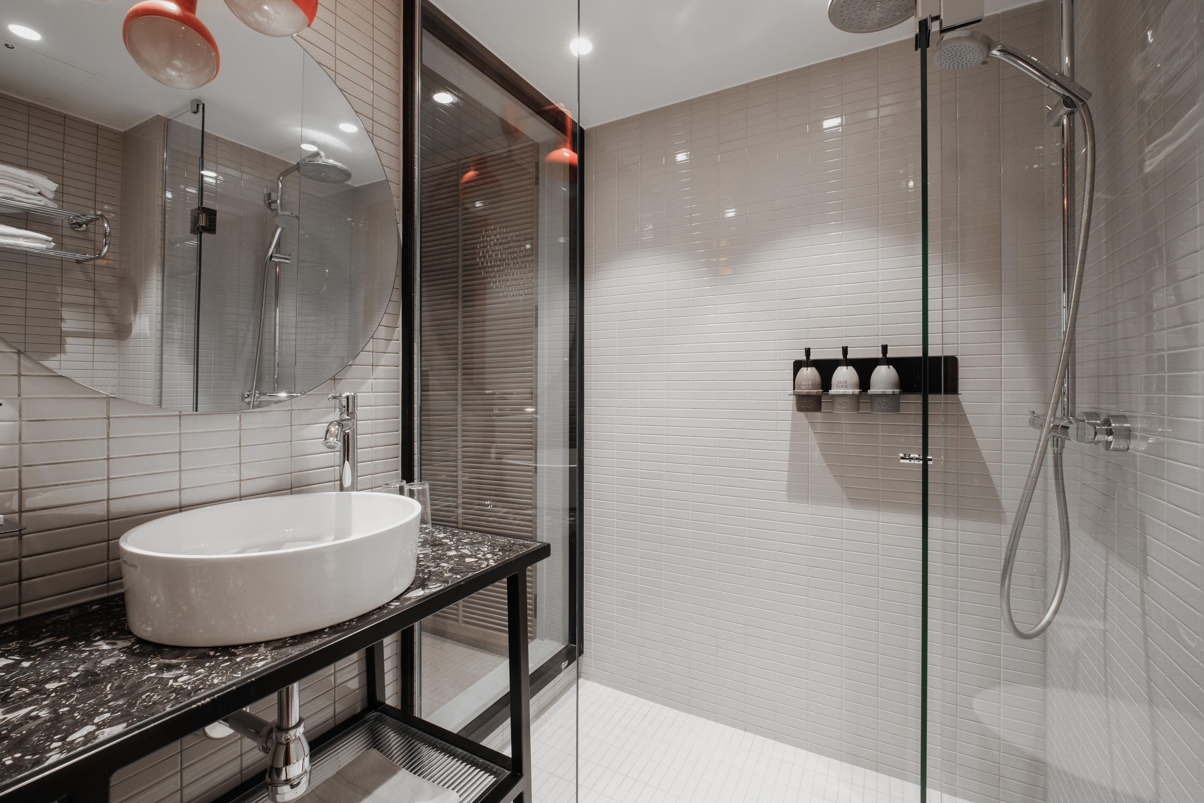 Rymligt badrum i grått kakel i ett Superiorrum på Hobo Hotel i centrala Stockholm, med dusch och hygienprodukter, modern, funktionell och stilren design med en tydlig urban känsla.