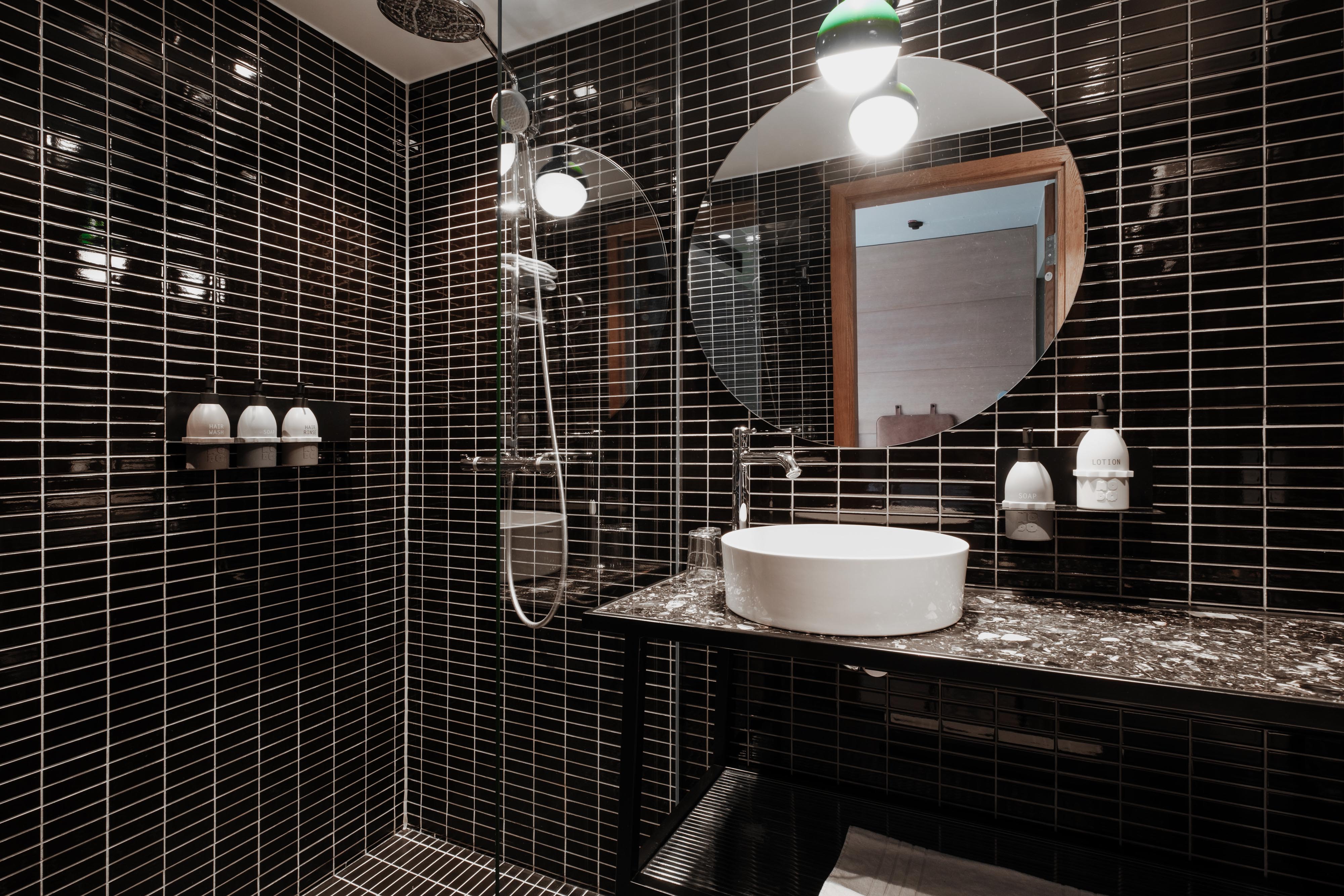 Rymligt badrum i svart kakel i ett Standardrum på Hobo Hotel i centrala Stockholm, med dusch och hygienprodukter, modern, funktionell och stilren design med en tydlig urban känsla.