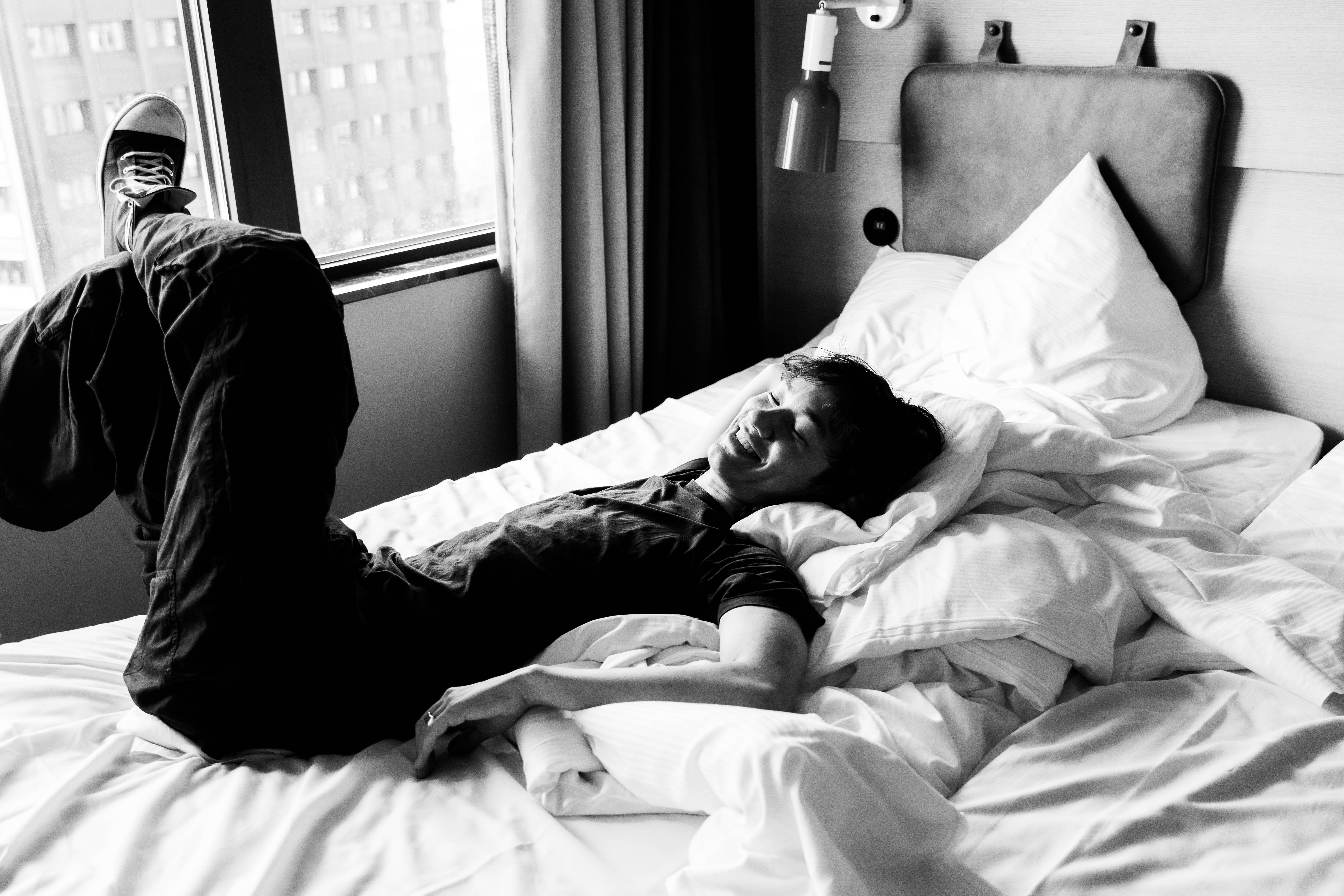 Gäst skrattar i en enkelsäng i ett Superior-rum på Hobo Hotel i centrala Stockholm, med utsikt över Brunkebergstorg.