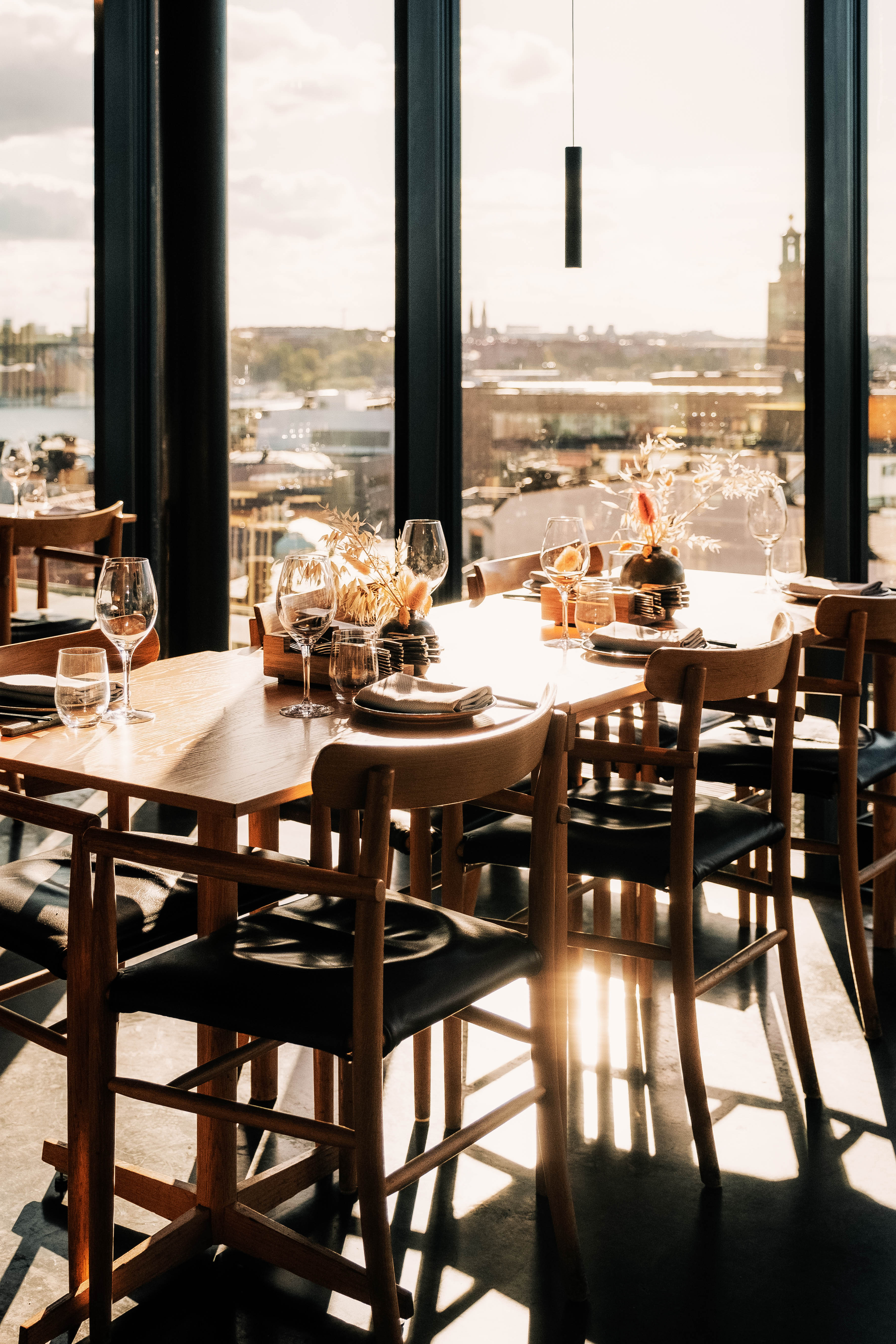 Set dining table in a restaurant at Hobo Hotel in central Stockholm, with large windows and views over the city skyline.