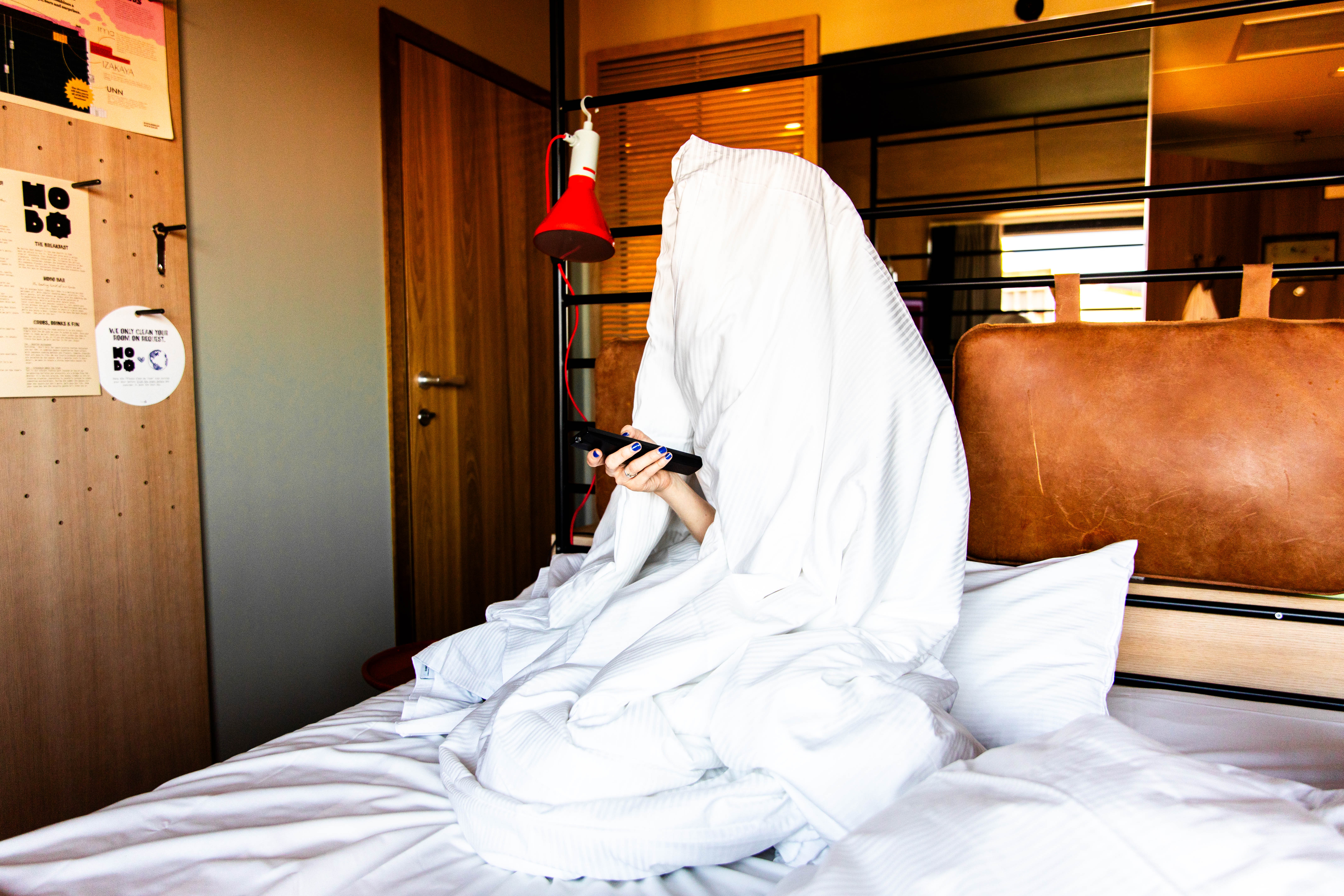 Guest under a blanket holding a remote in a Superior hotel room at Hobo Hotel in central Stockholm.