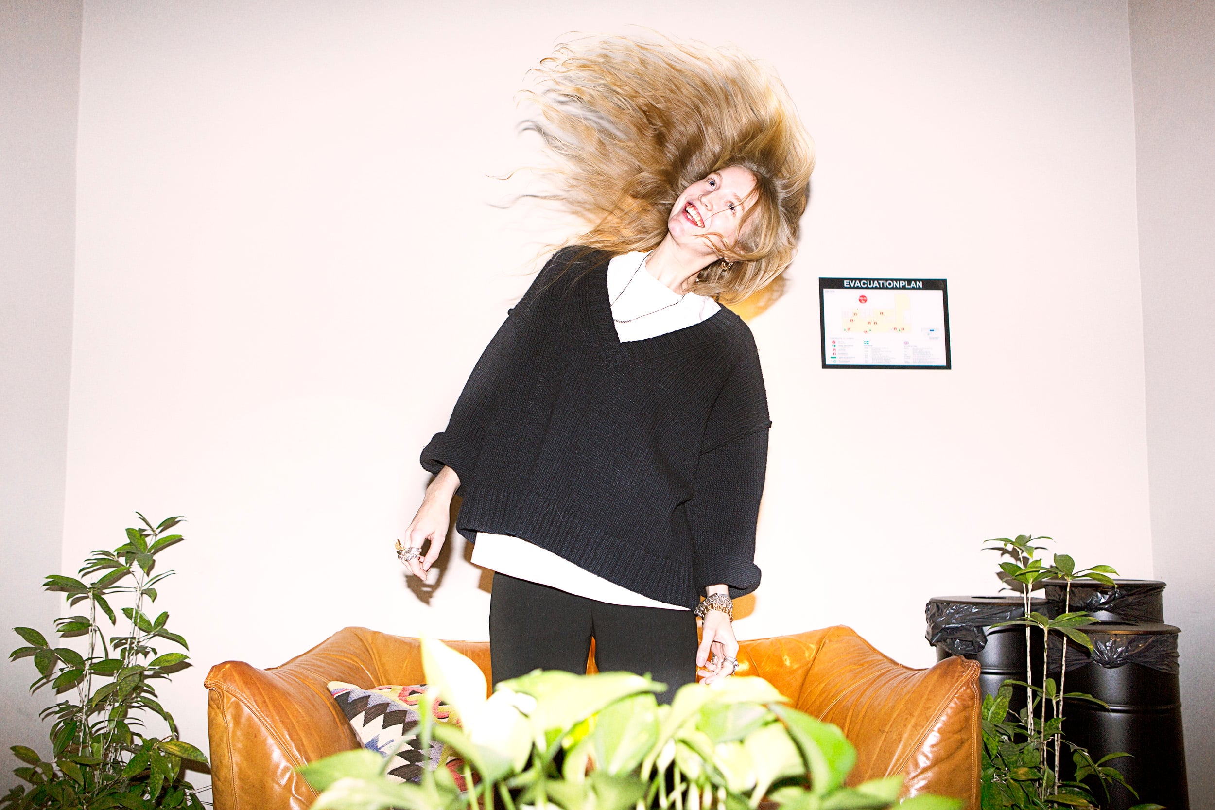 Glad tjej som slänger med håret framför en skinnsoffa, med en grön planta i bakgrunden, på Hobo Hotel i centrala Stockholm.