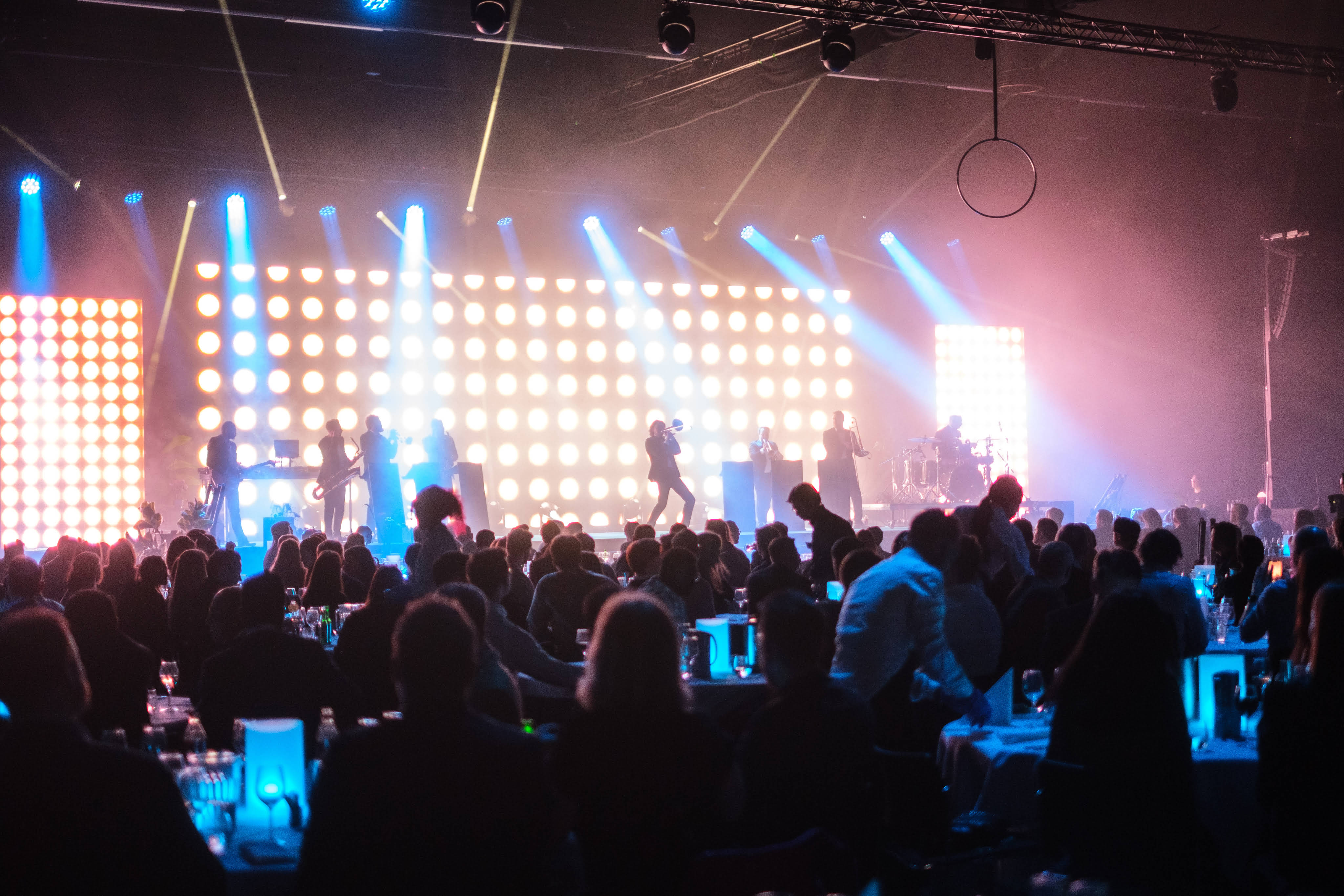 The Qube - A group of people on stage with lights and people sitting around