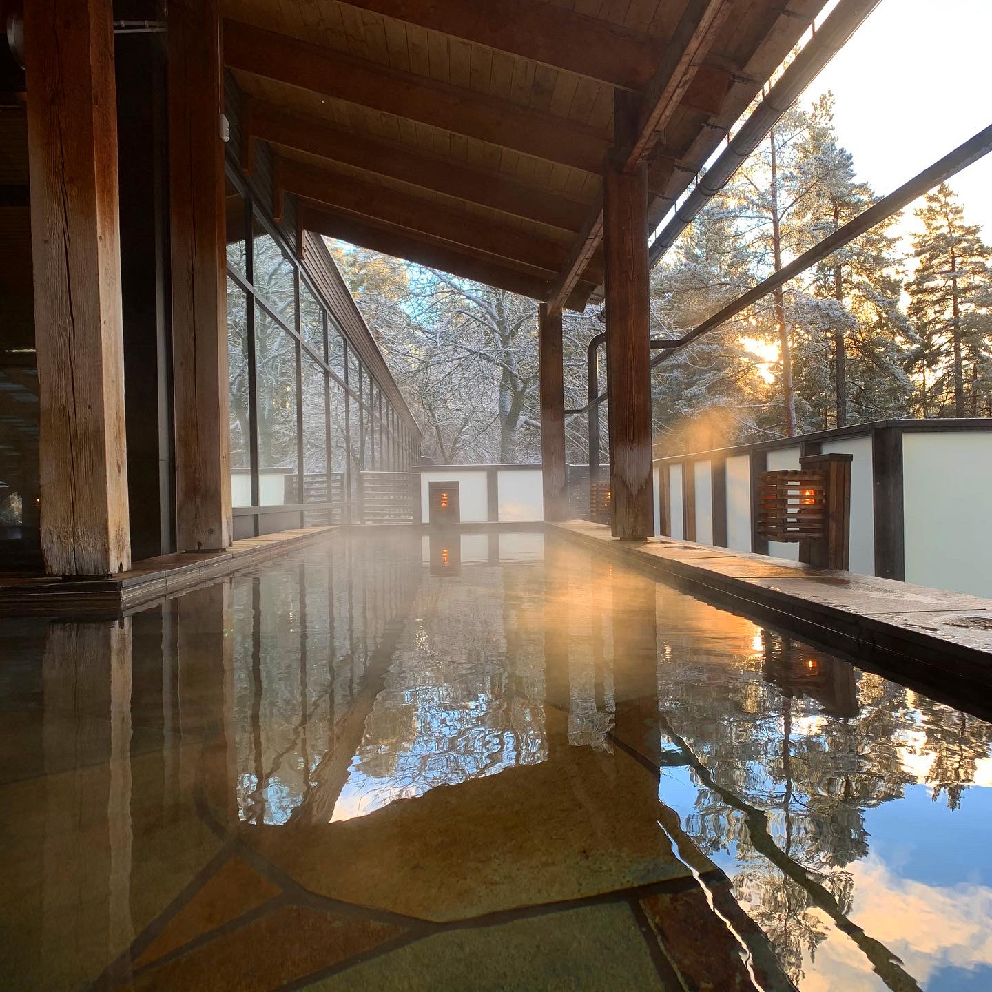 Varm källa utomhus omgiven av frostiga träd och solsken som strilar genom träden och speglar sig i vattnet, Bild från japanska badet på Yasuragi Spa